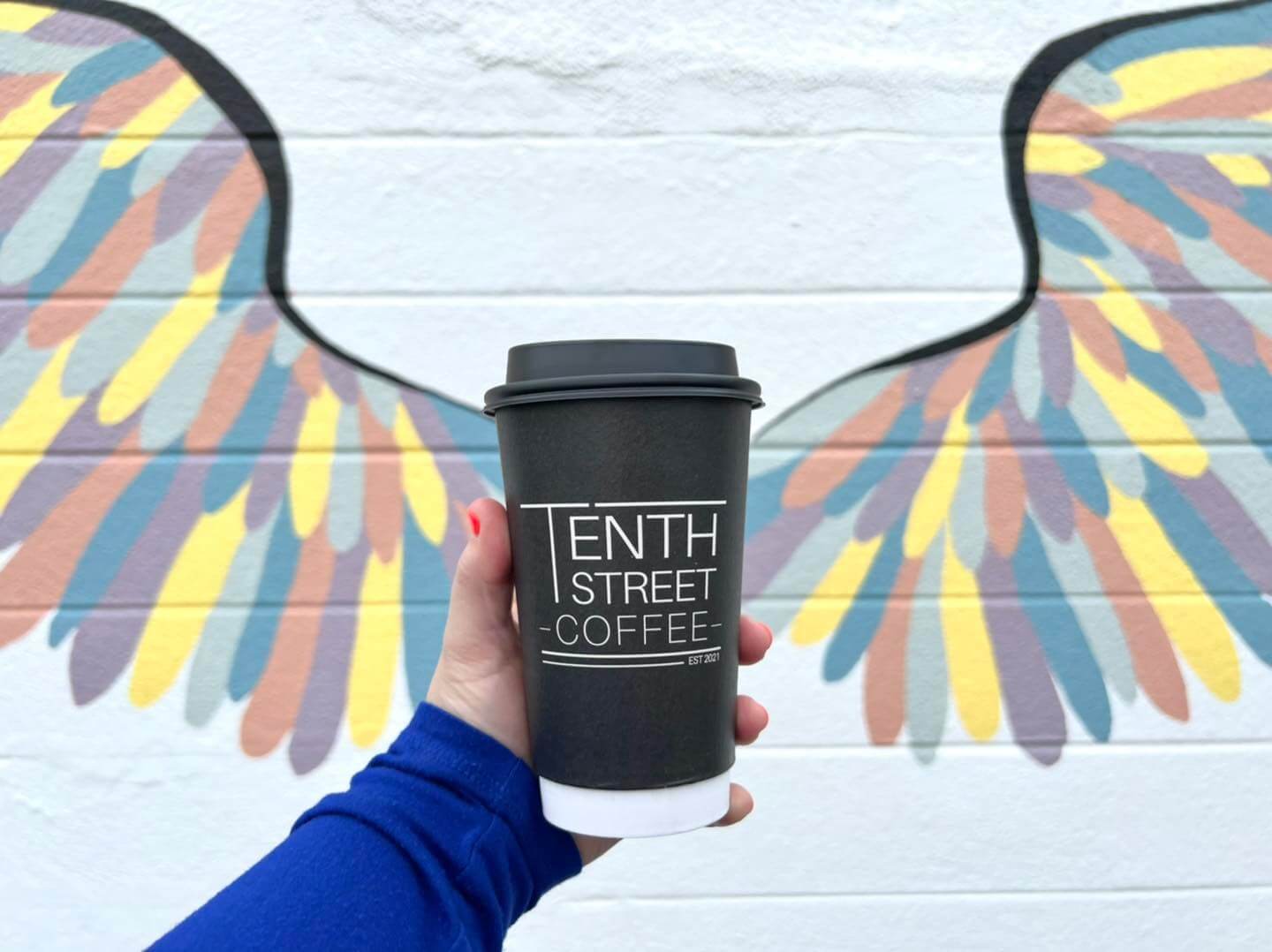 a hand holding a coffee cup with a winged mural in the background