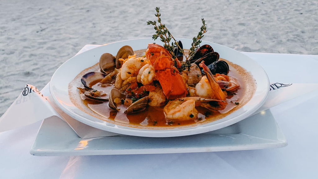 bowl of seafood dish sitting on a table on the sand of a beach