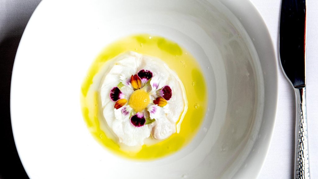 fancy floral dish on a white bowl with a yellow puree and white flowers