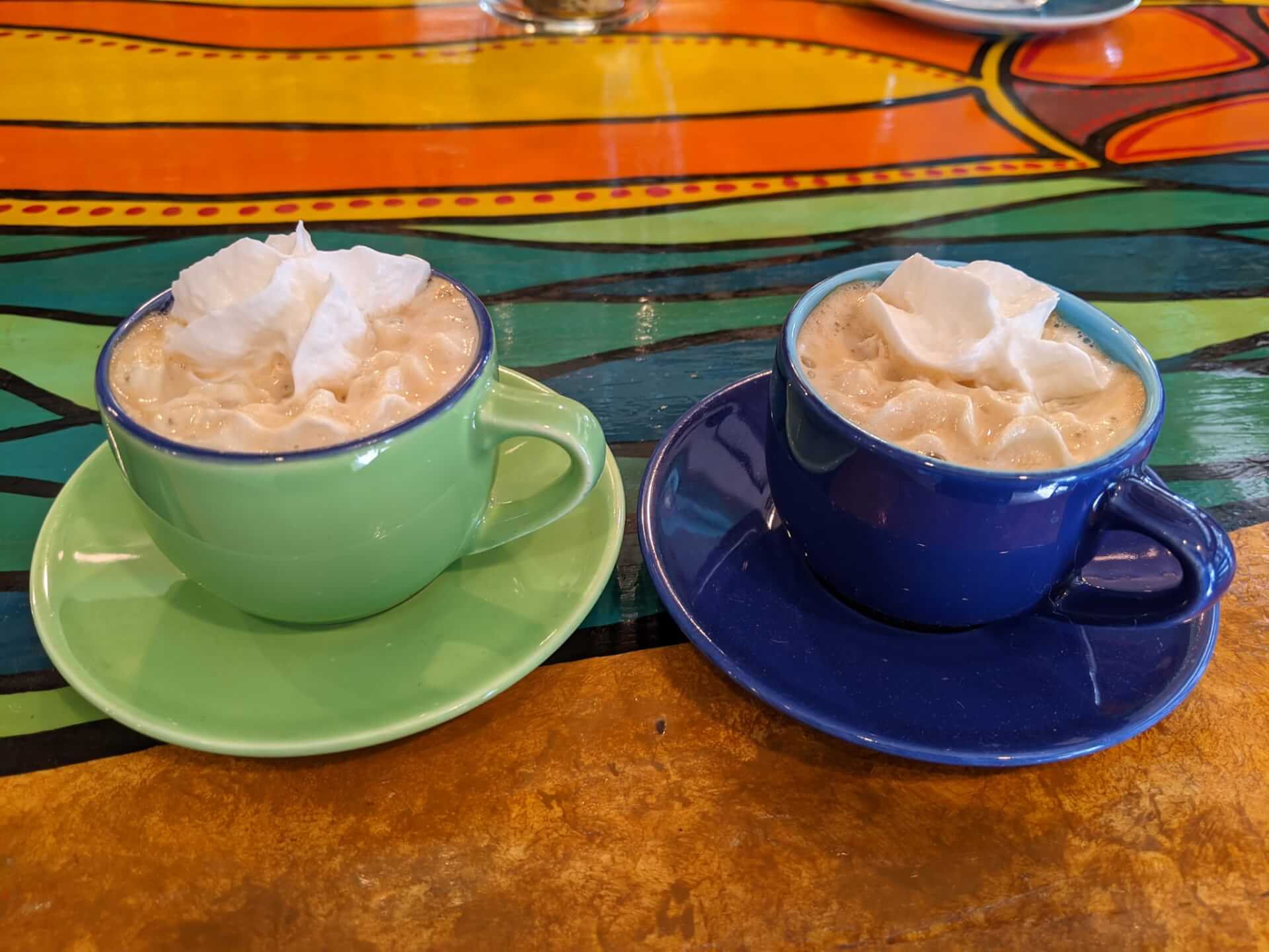 two cups of coffee with whipped cream on colorful saucers