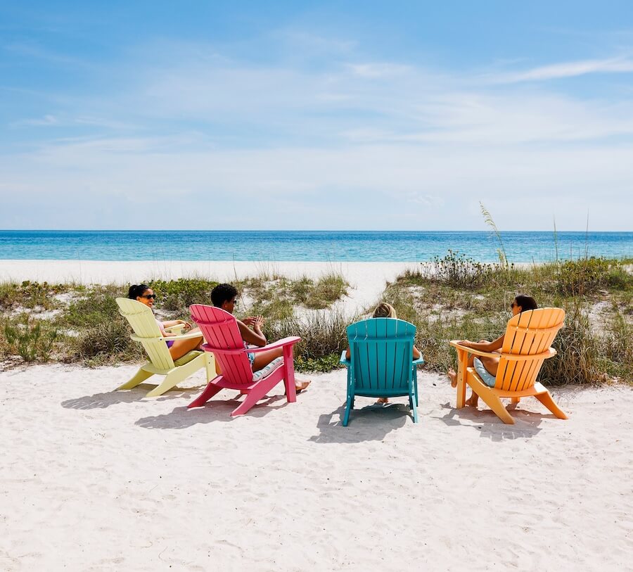 women sitting in colorful chairs on the beach looking at the water