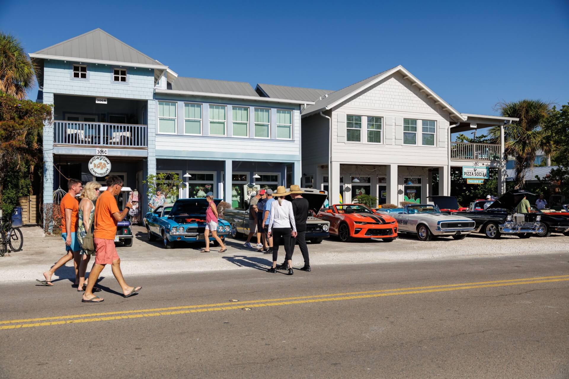 a group of people walking on the street with vintage cars parked