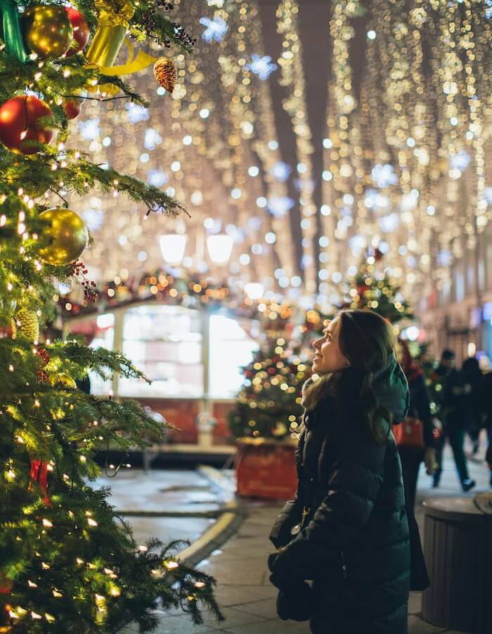 a woman standing next to a christmas tree with lights all around